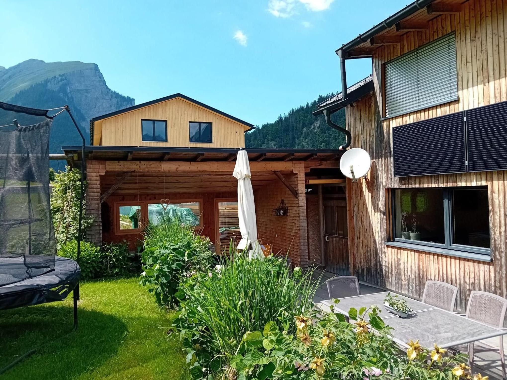 A wooden cabin with a patio, a trampoline, and a mountain backdrop.