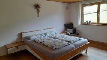 Een slaapkamer met een houten bed, een stoel, een raam en een decoratie aan de muur.