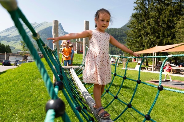 Un nen jugant en un pont de corda a un parc amb muntanyes al fons.