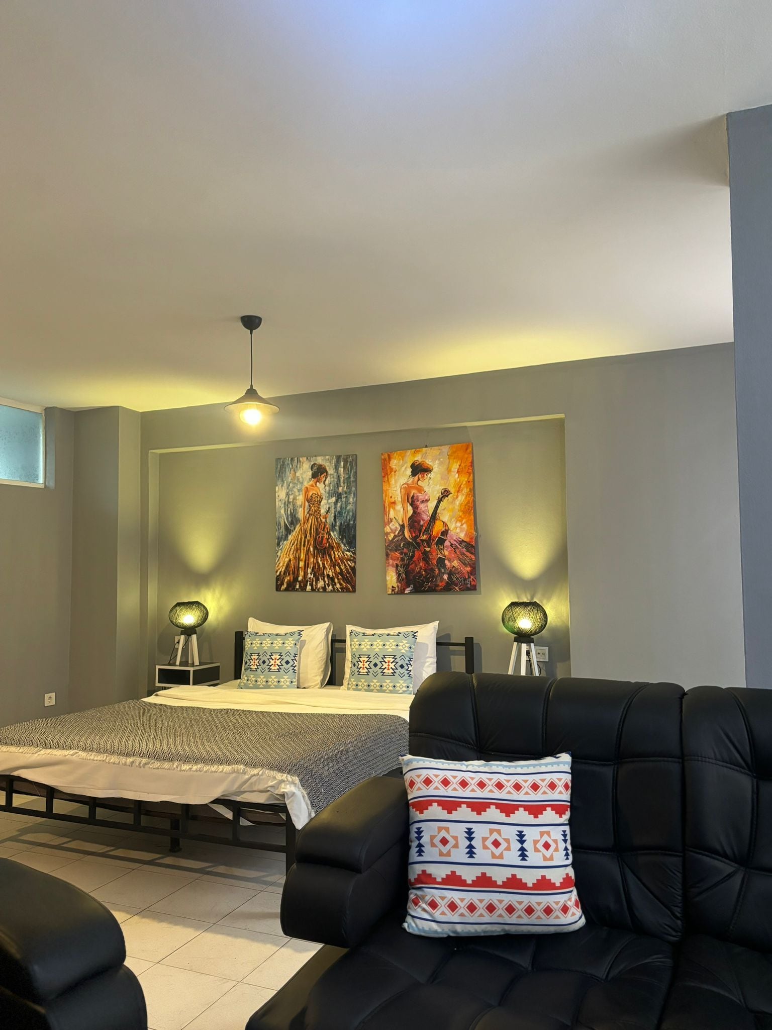 Un dormitorio moderno con una cama, dos lámparas de pared y dos cuadros.