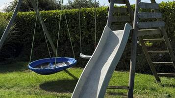 Un ensemble de jeux d’extérieur en bois, comprenant un toboggan et une balançoire suspendue, installé dans un espace herbeux.