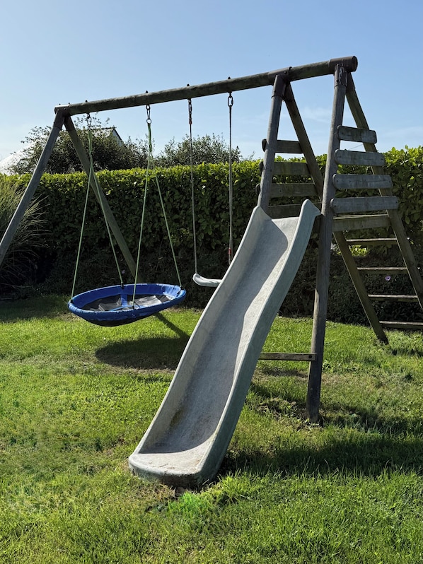 A wooden swing set with a slide and a hanging swing in a grassy area. - Vrbo Property (Landéda)