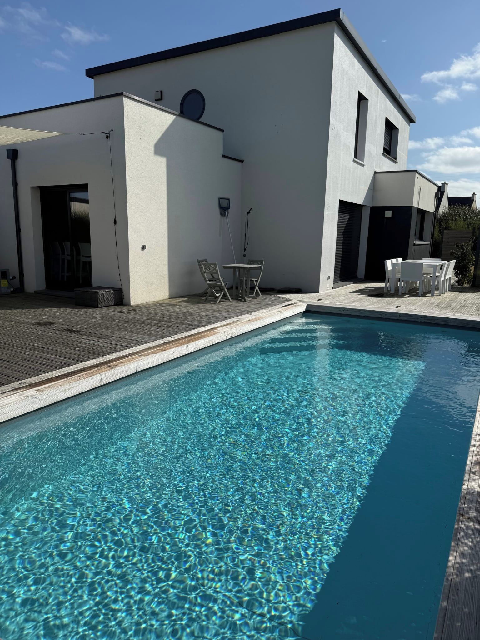 Ein modernes Gebäude mit Schwimmbad, Sitzgelegenheiten im Freien und blauem Himmel.