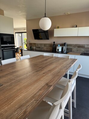 Eine moderne Küche mit einem Holztisch, weißen Stühlen, einer Hängelampe und einem Einbauofen.