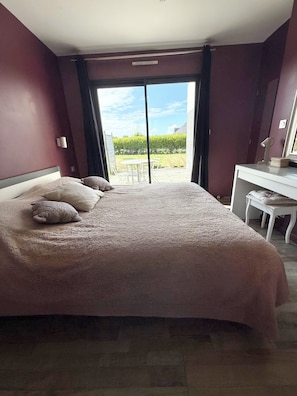 A bedroom with a large bed, a desk, and a view of a garden through a sliding door. - Vrbo Property (Landéda)