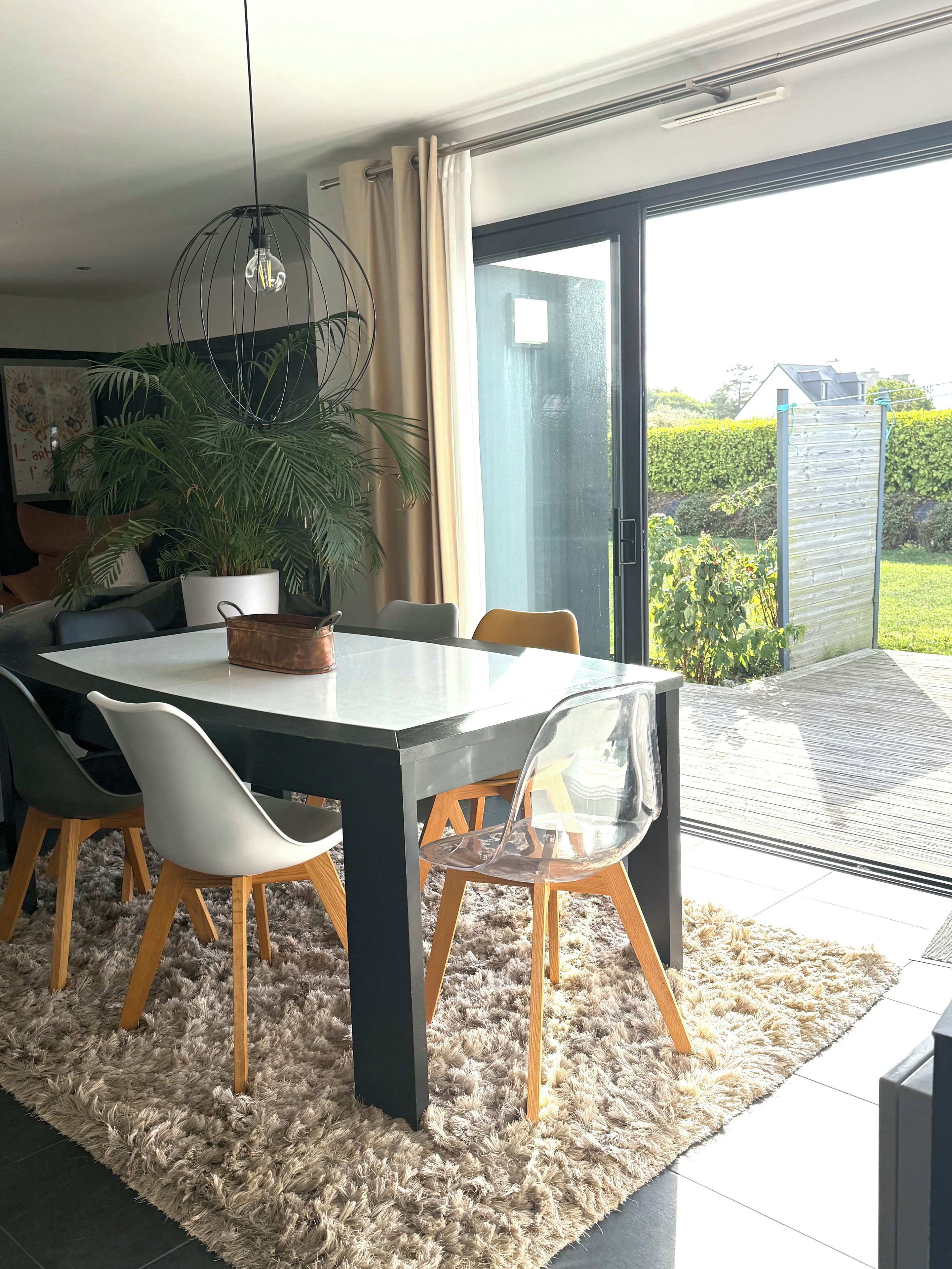 Een moderne eetruimte met een ronde tafel, stoelen, een potplant en een uitzicht door een glazen deur naar buiten.