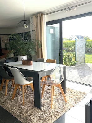 A modern dining area with a round table, chairs, a potted plant, and a view through a glass door to the outdoors. - Vrbo Property (Landéda)