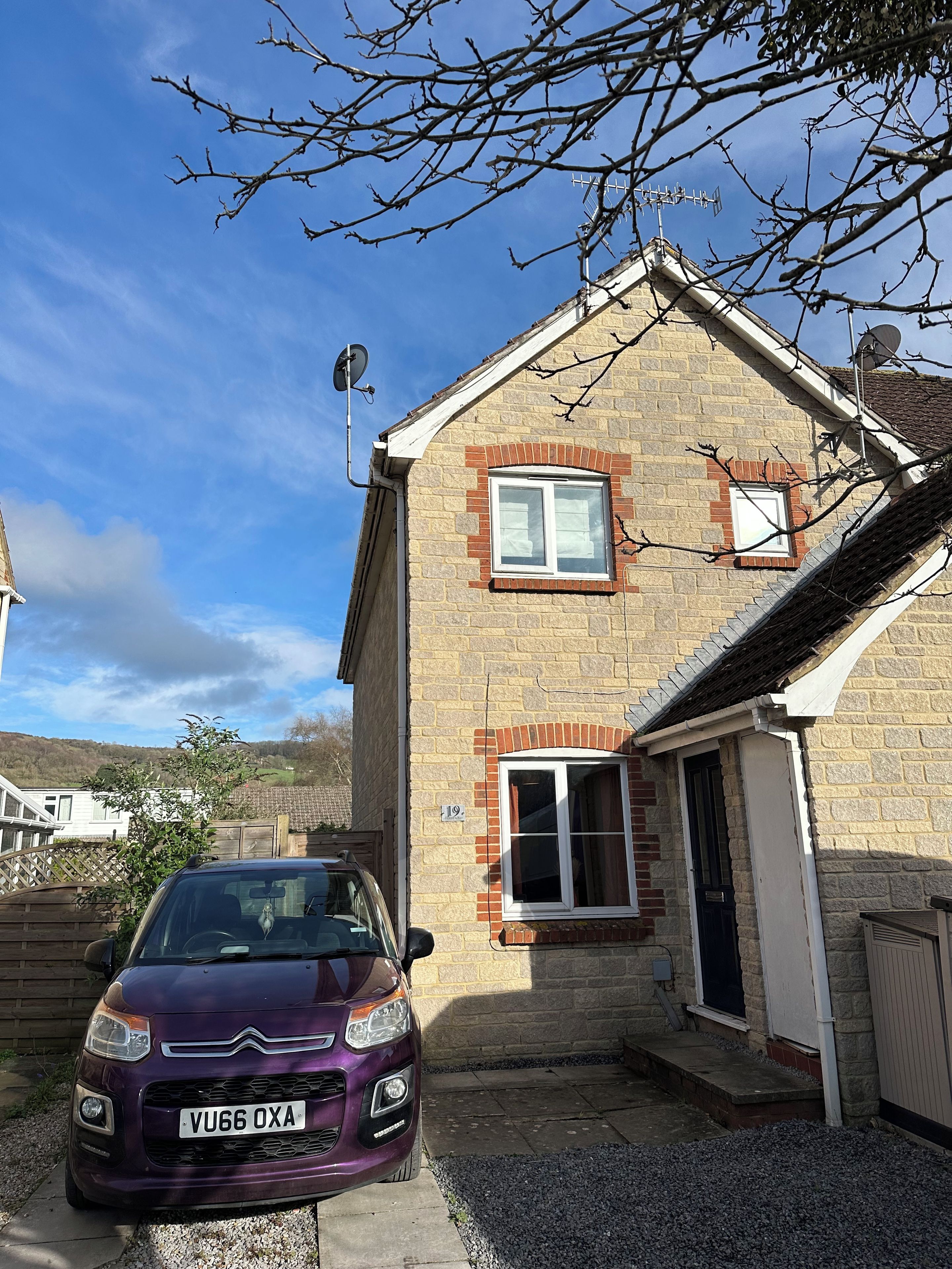 A two-story house with a brick facade, a satellite dish, and a car parked in the driveway.