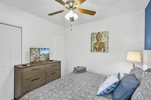 A bedroom with a bed, a dresser, a television, a ceiling fan, a wall-mounted Buddha statue, and a lamp. - Lovely 1 Bed 1 Bath Apt Minutes to the Beach, Pool (Lauderdale-by-the-Sea)