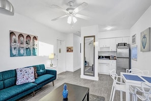 A modern living room with a teal sofa, a coffee table, and a dining area with white chairs. - Lovely 1 Bed 1 Bath Apt Minutes to the Beach, Pool (Lauderdale-by-the-Sea)