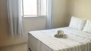 Un dormitorio con una cama, una ventana con cortinas y una toalla enrollada sobre la cama.