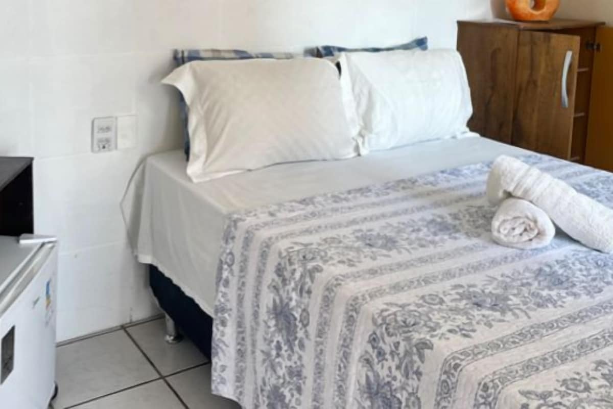 Una cama individual con un edredón estampado, un armario de madera y un pequeño escritorio con silla.