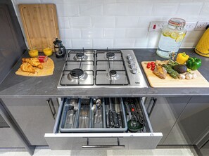 A kitchen with a gas stove, a cutting board with food items, and a drawer with utensils. - Den Duplex | 3BR | Sleeps 6 | Free Parking (Rugby)