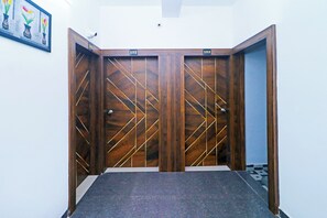 Un juego de puertas dobles de madera con un diseño geométrico, una placa con un número encima y una pequeña cámara de seguridad en la pared.