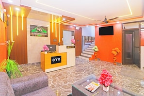 Zona de recepción de un hotel con un mostrador de recepción identificado con 'OYO', un cartel que indica 'Hotel MG International' y una escalera que sube a un piso superior.