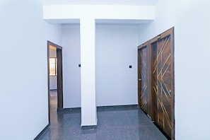 Passadís amb un pilaret blanc, una porta de fusta amb dibuixos geomètrics i una porta amb un número.