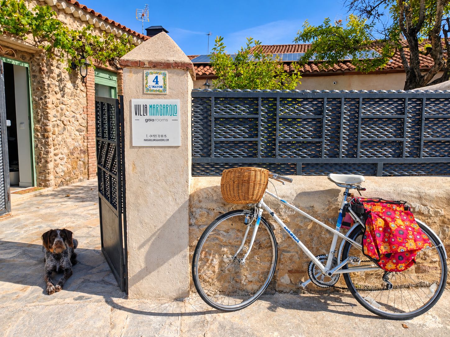 Un edificio de piedra con un cartel que dice 'VILLA MARGAROYO' y una bicicleta con cesta y una bolsa colorida.