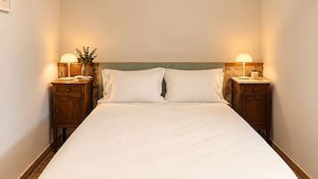 Una cama bien hecha con sábanas blancas, dos mesitas de noche con lámparas, un cabecero de madera y un aplique de techo tejido.
