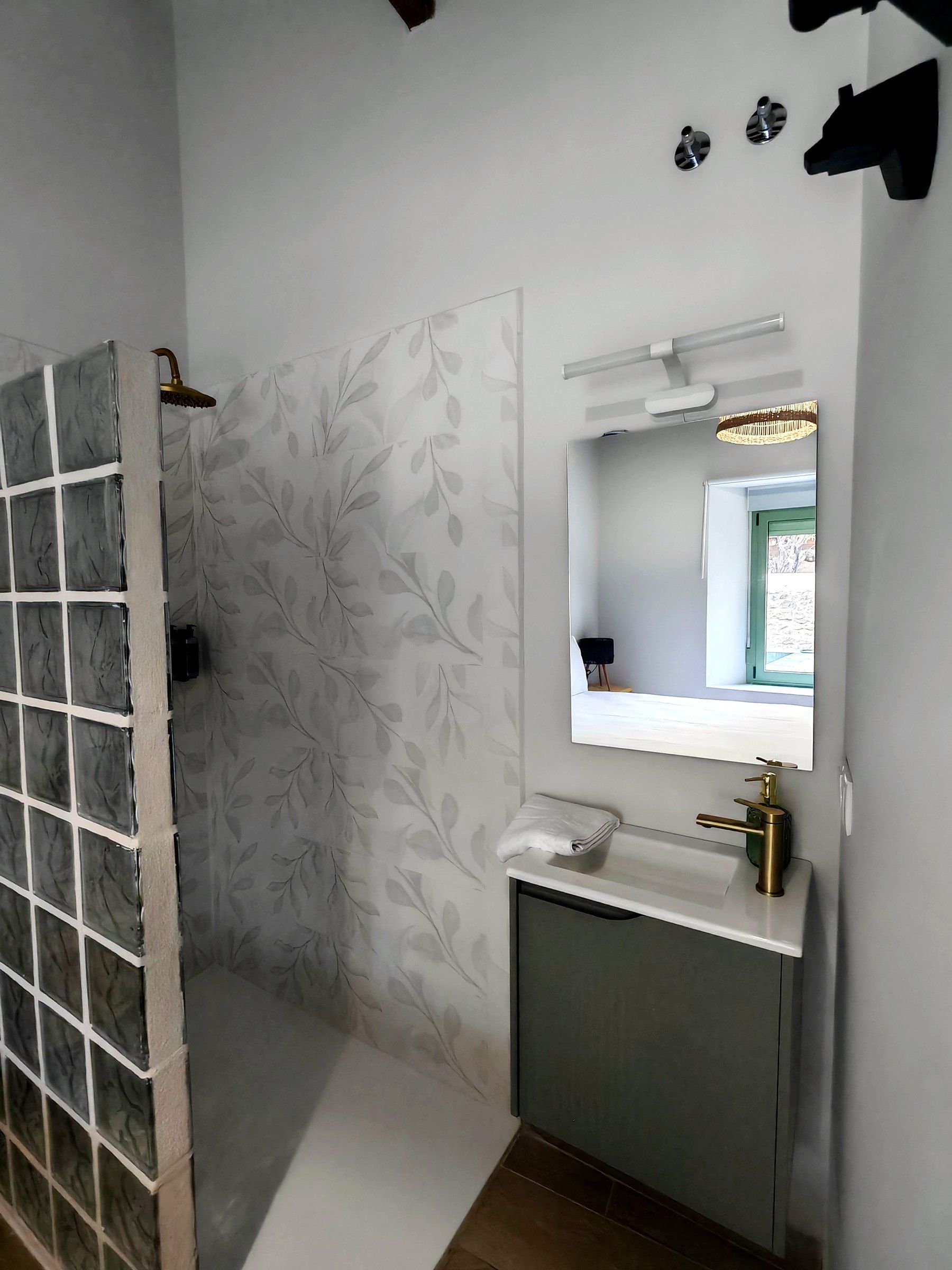 Een badkamer met een douche, een wastafel met spiegel en een behang met patroon.