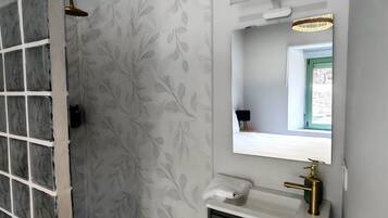 Een badkamer met een douche, een wastafel met spiegel en een behang met patroon.