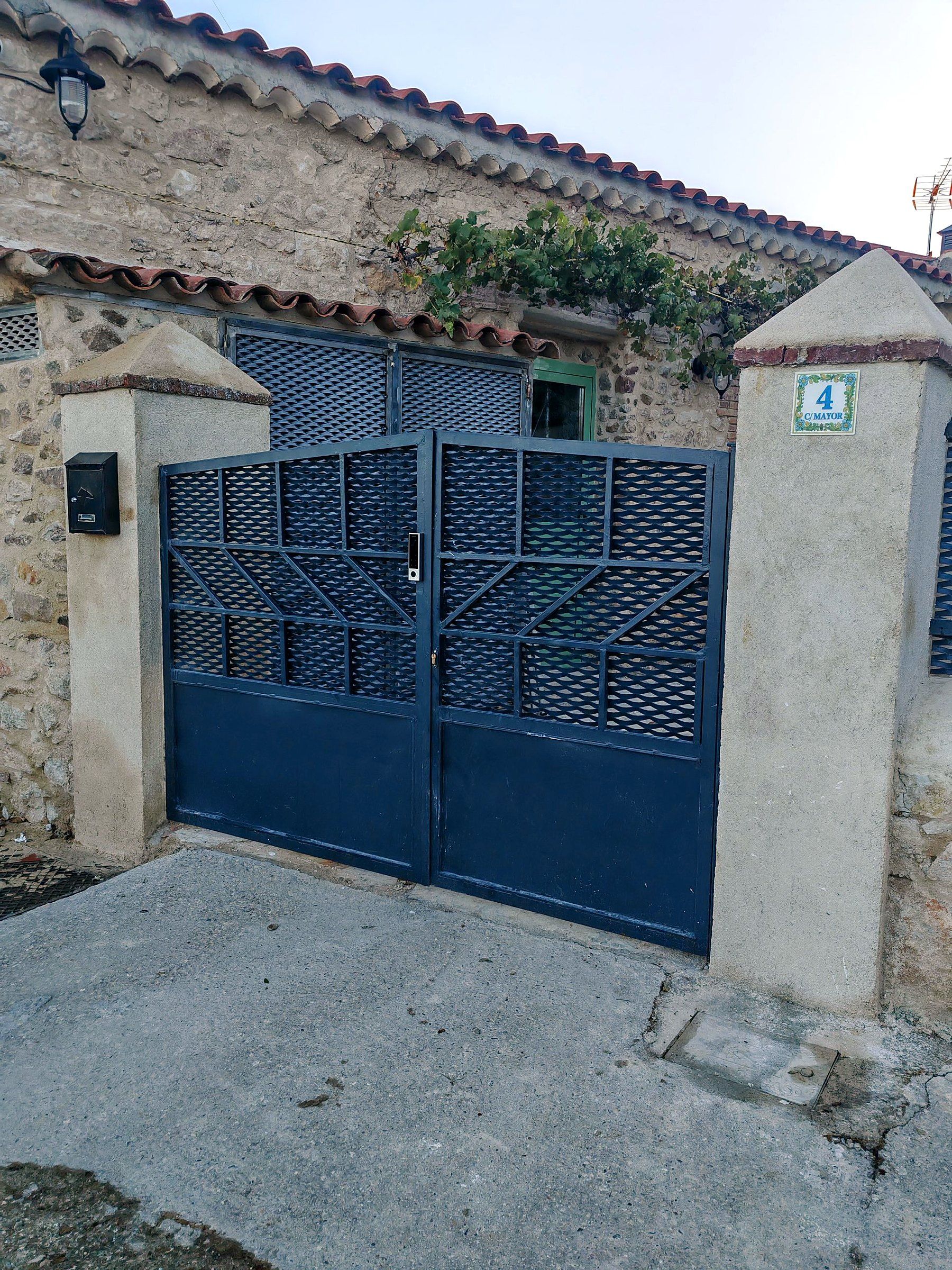 Una entrada protegida con una verja metálica y un buzón en la pared.