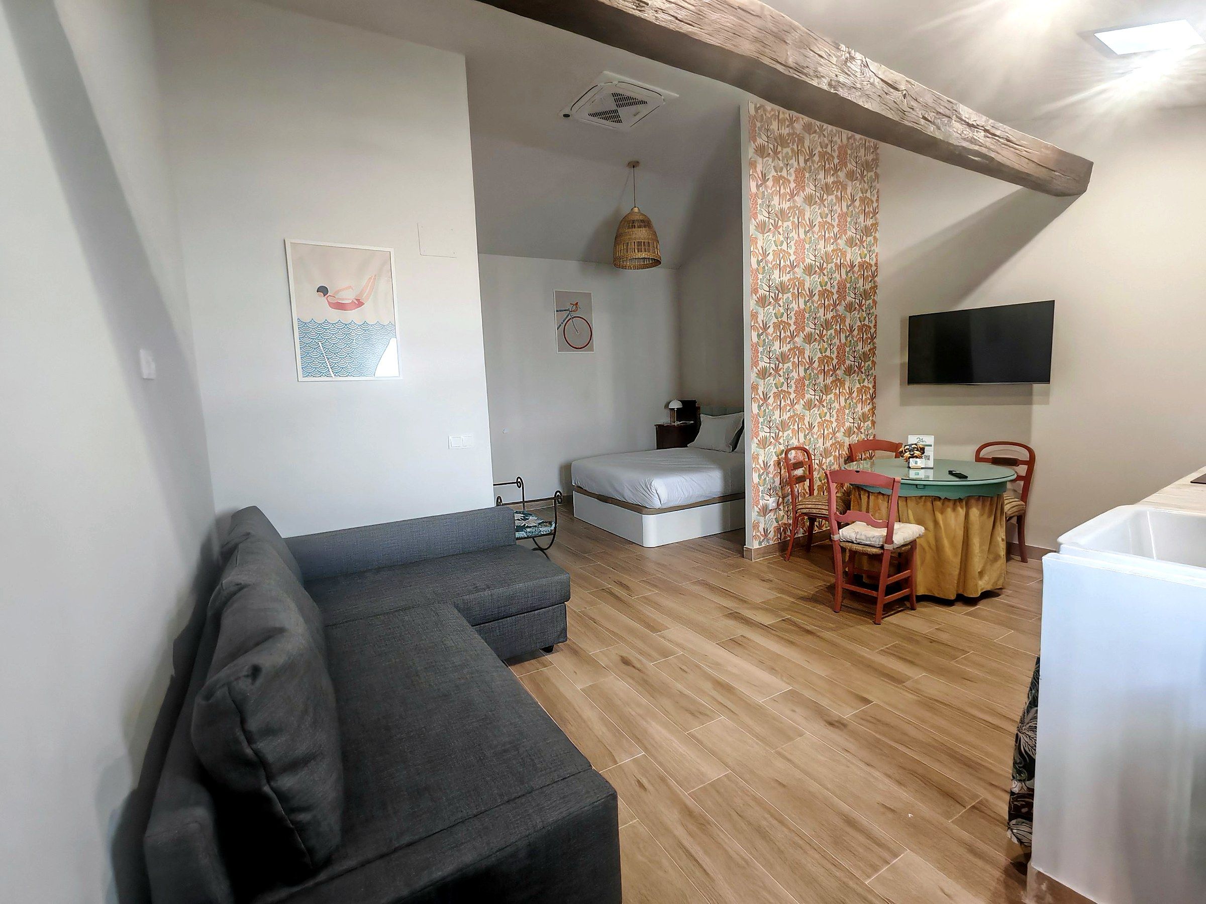 Una sala de estar moderna con un sofá gris, un comedor con mesa y sillas, una cama y un televisor montado en la pared.