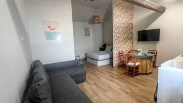 Una sala de estar moderna con un sofá gris, un comedor con mesa y sillas, una cama y un televisor montado en la pared.