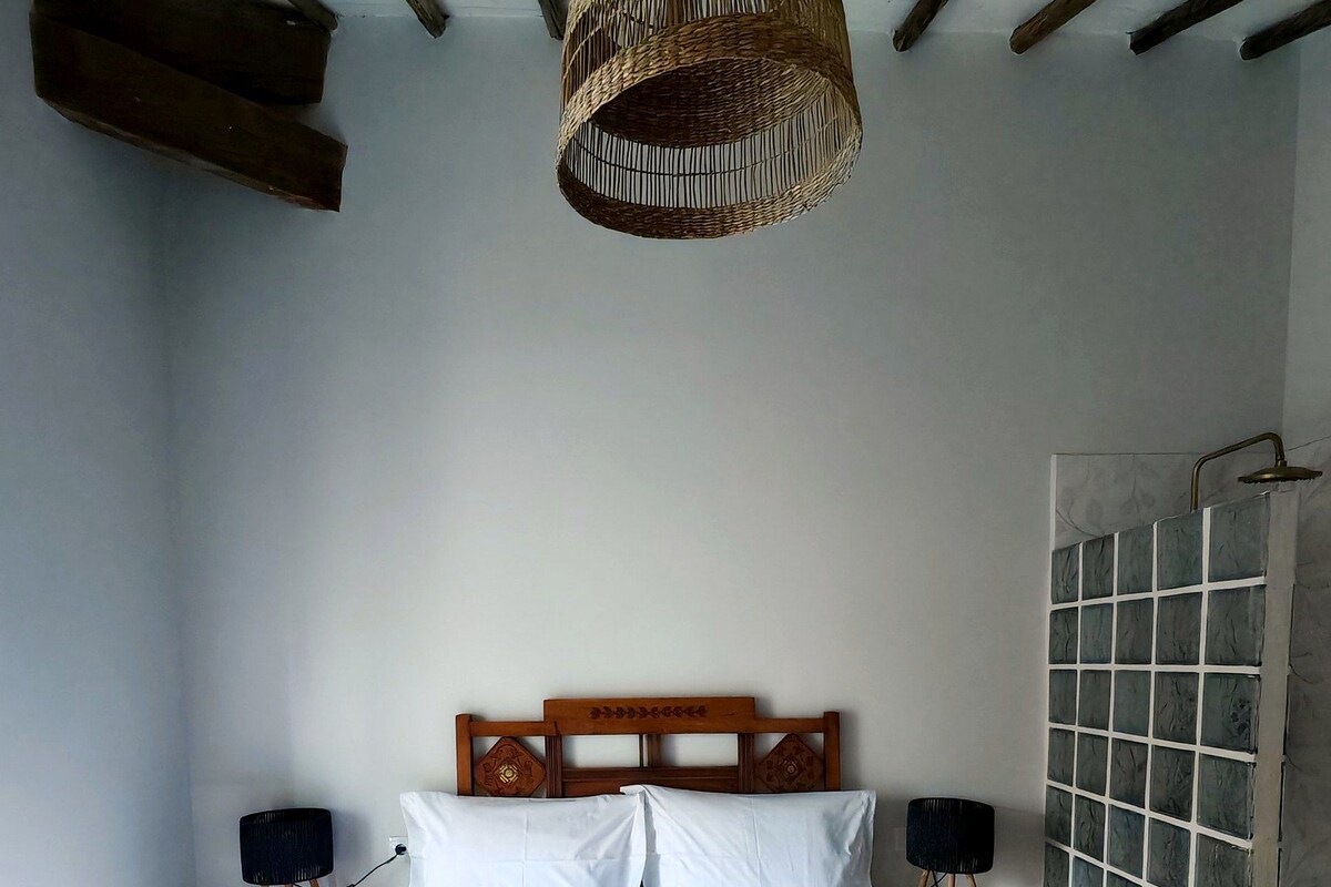 A bedroom with a large bed, wooden headboard, bedside tables with lamps, and a hanging light fixture.