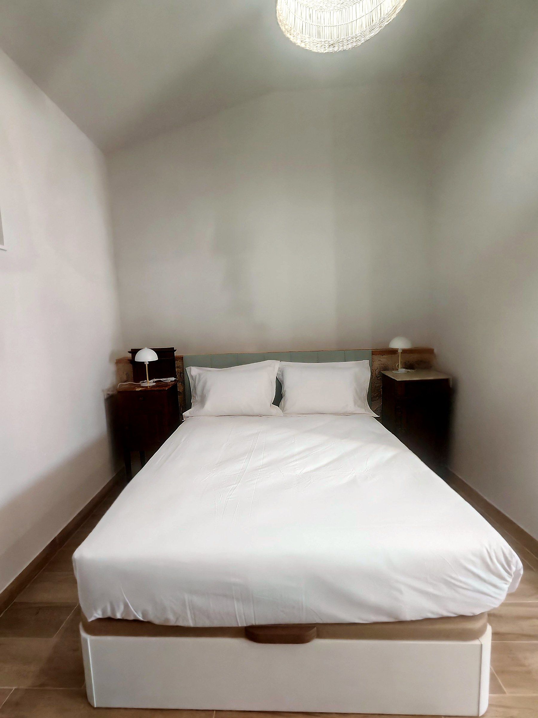 Una cama bien tendida con sábanas blancas en una habitación con paredes lisas y un diseño sencillo y moderno.