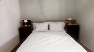 Una cama bien tendida con sábanas blancas en una habitación con paredes lisas y un diseño sencillo y moderno.