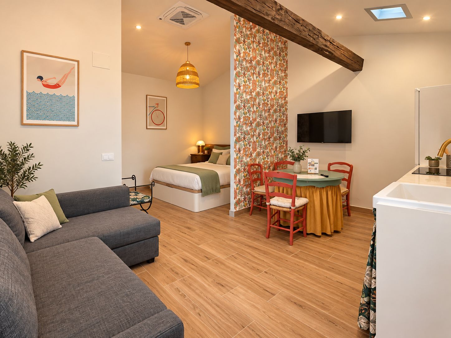 Een moderne woonkamer met een bank, een eethoek met stoelen, een bed, een televisie en een keuken met een spoelbak.