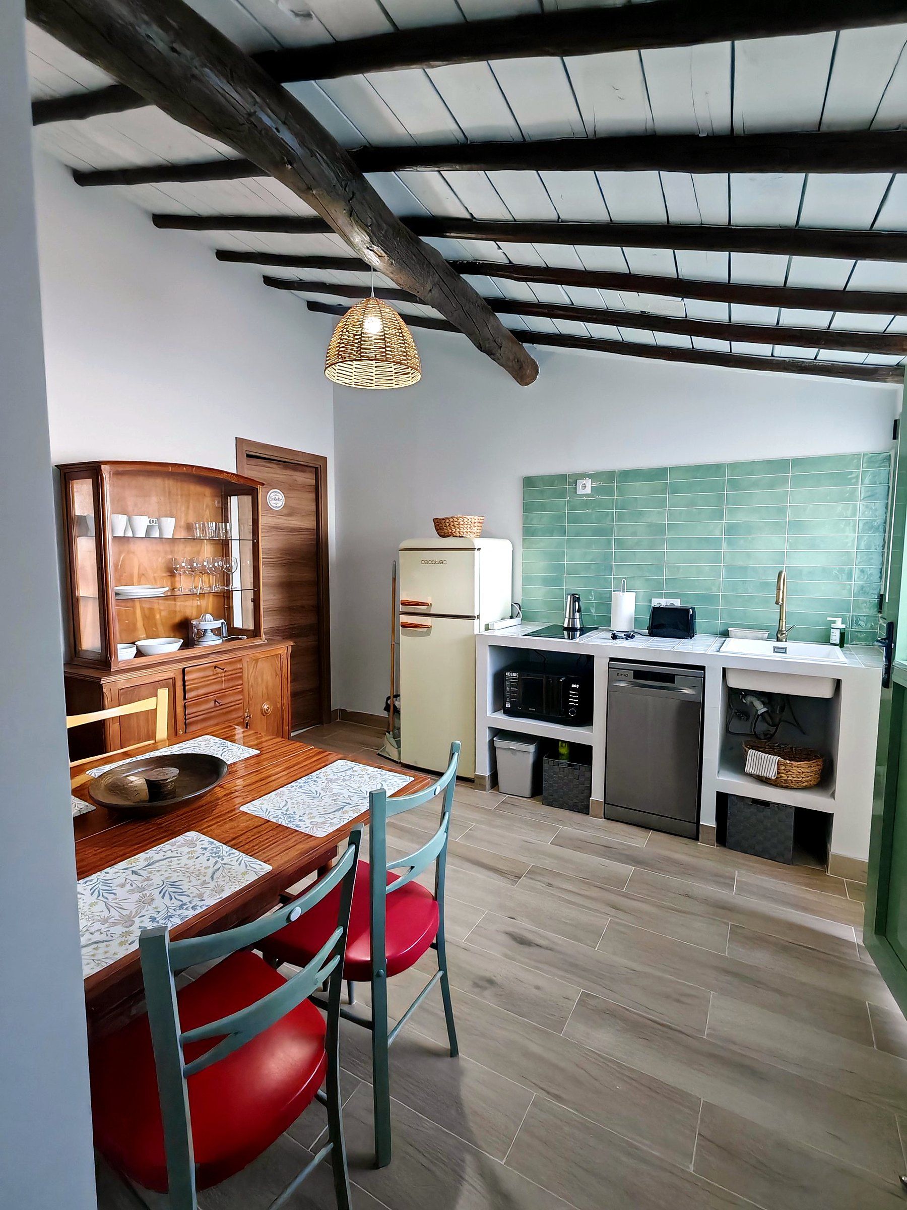 Una cocina compacta con armarios de madera, una mesa de comedor con sillas y una lámpara colgante.