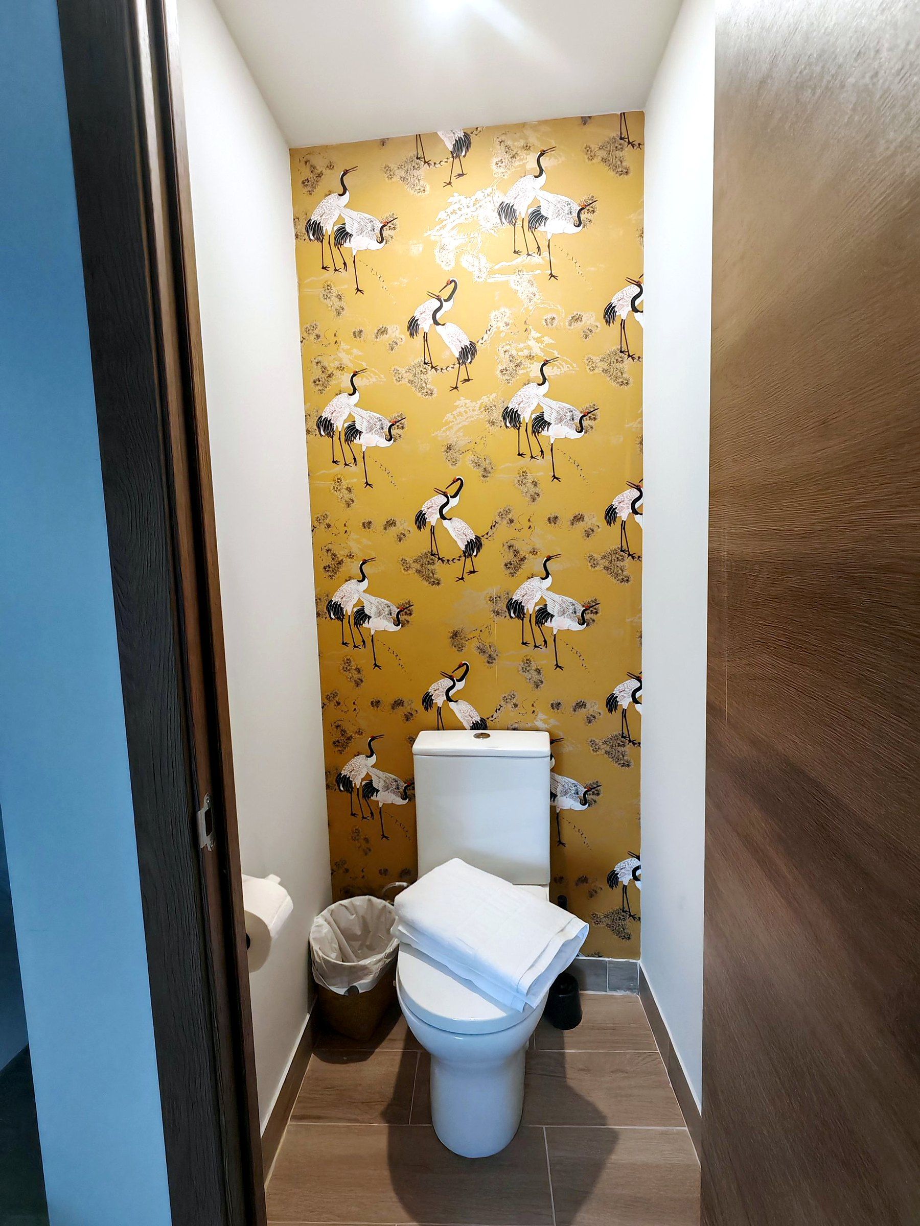 A small bathroom with a toilet, a trash bin, and a wall with a pattern of birds.