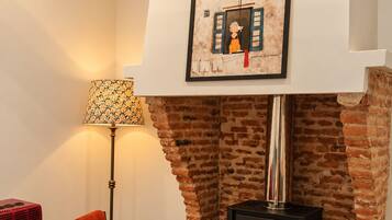 Una habitación acogedora con chimenea de ladrillo, un cuadro colgado encima, una silla roja, una lámpara de pie y un calefactor rojo.