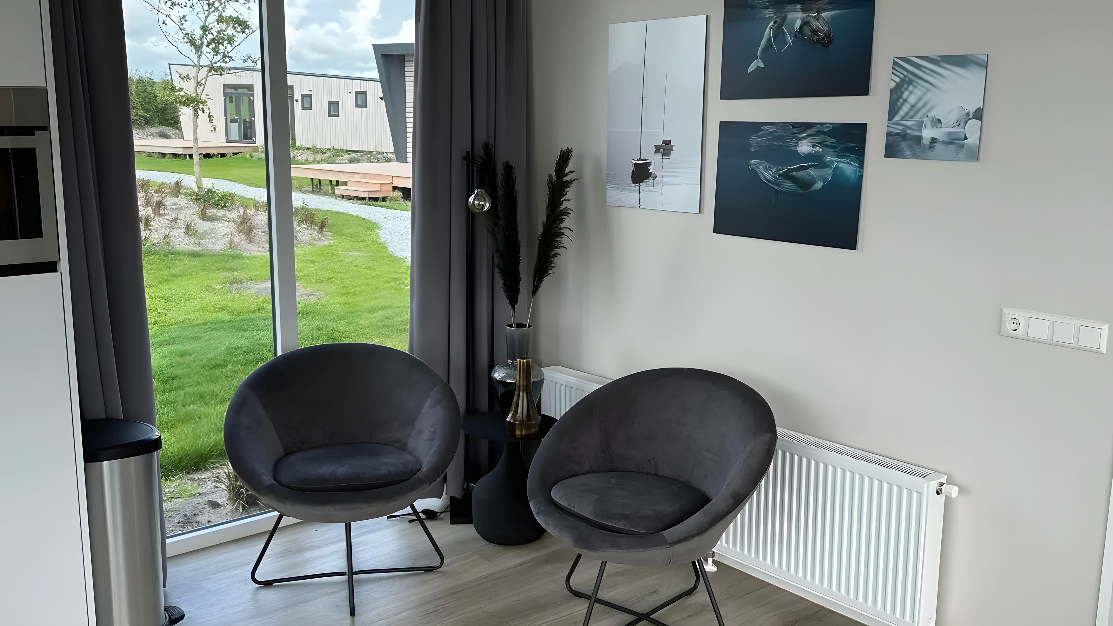 Une pièce moderne avec deux fauteuils gris, un radiateur et une vue sur un immeuble et la verdure environnante.