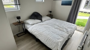 Ein Schlafzimmer mit einem Bett, zwei Nachttischen, einem Fenster und Blick ins Freie.