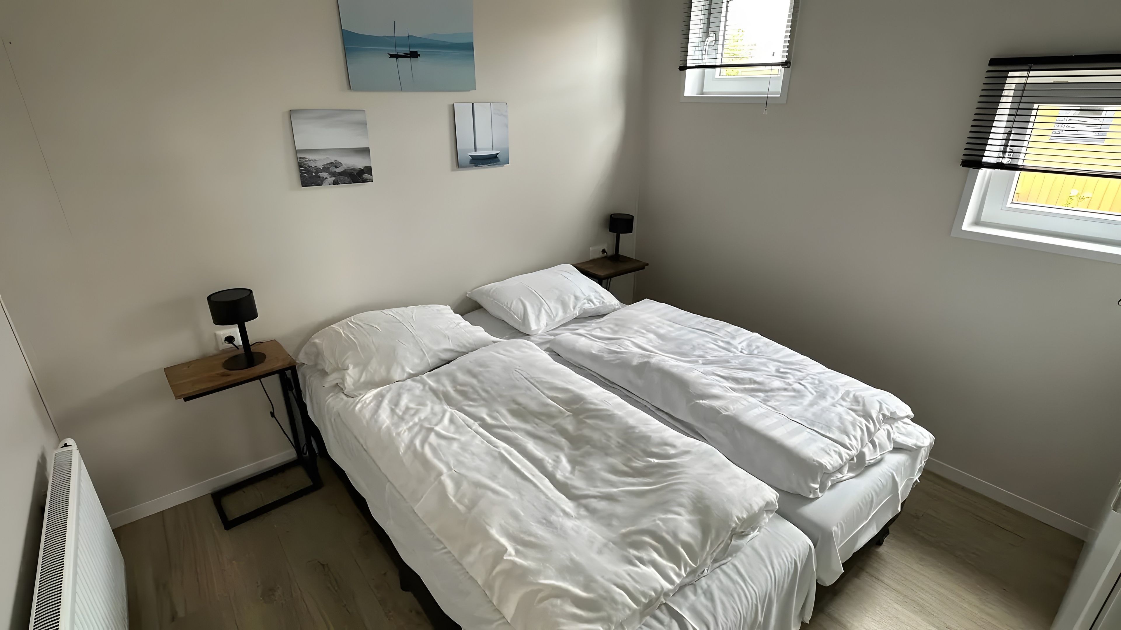 Quarto com duas camas, uma mesa de cabeceira com abajur e uma janela com persianas.