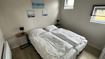 Quarto com duas camas, uma mesa de cabeceira com abajur e uma janela com persianas.