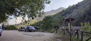 A gravel parking area with cars parked, surrounded by lush greenery and a mountainous backdrop.