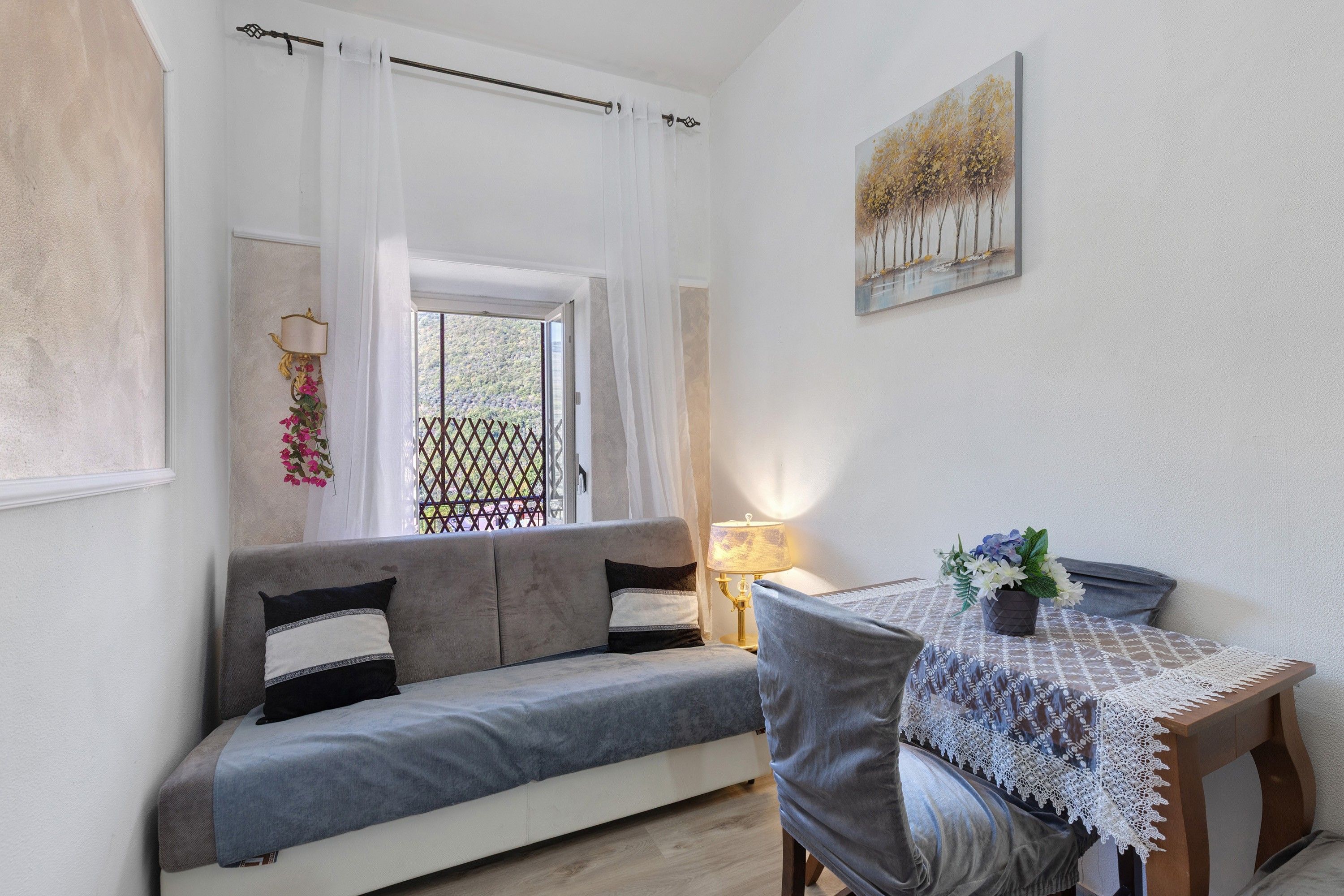 Una habitación acogedora con un sofá, una mesa con mantel de encaje y un cuadro en la pared.