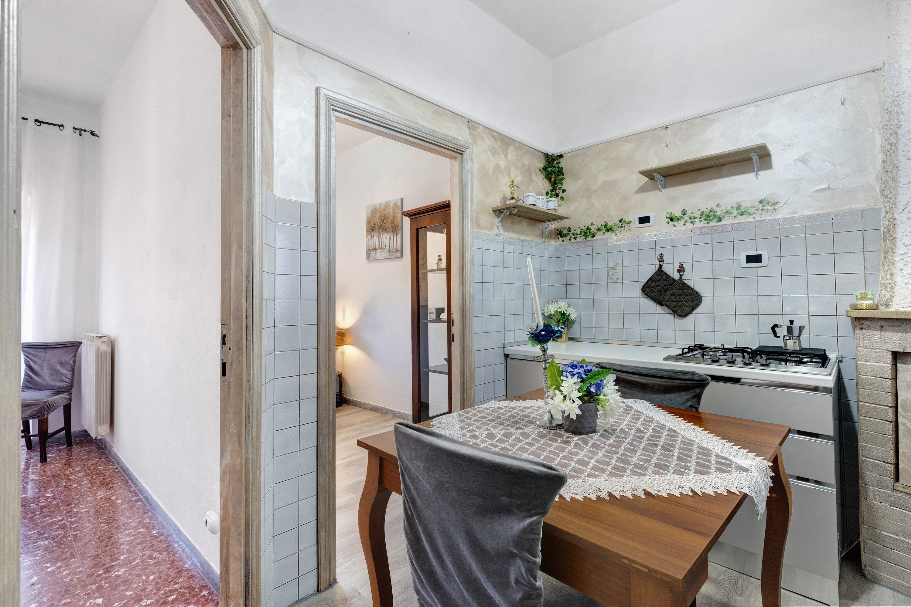 A compact kitchen with a dining area, featuring a stove, sink, and a small shelf with decorative items.