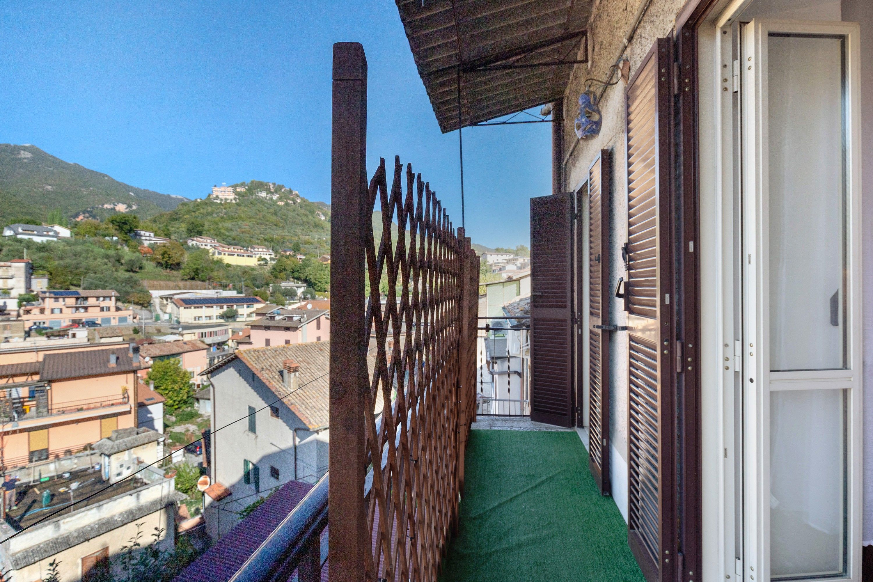 A balcony with a view of a hillside town, a wooden fence, and a door.