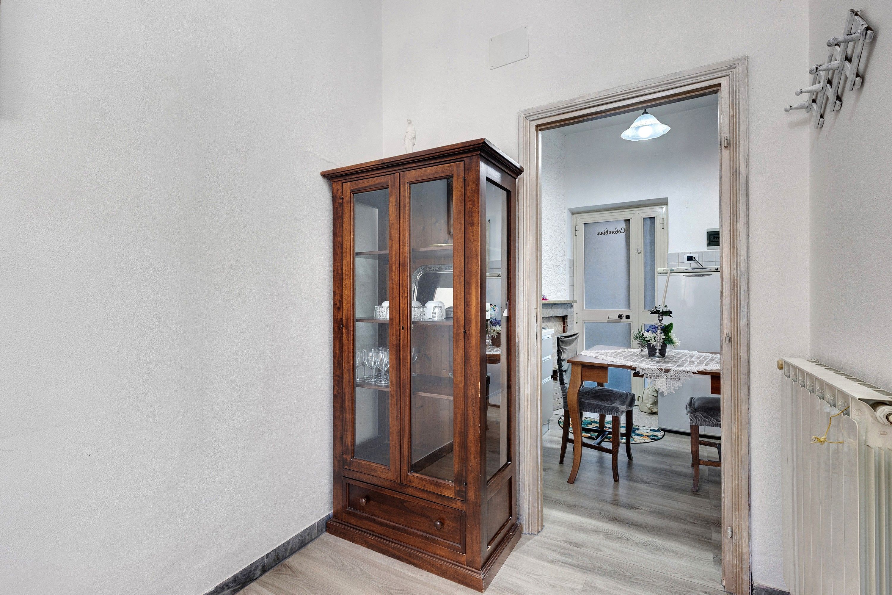 A narrow hallway with a wooden cabinet and a dining area with a table and chairs.