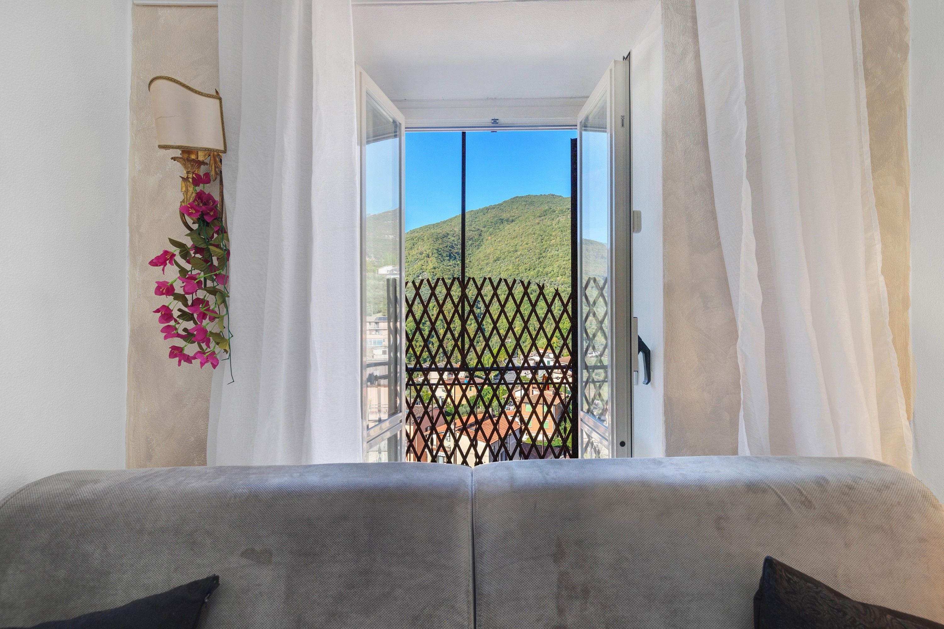 A bedroom with a bed, a view of a mountain through a window, and a balcony with a metal railing.