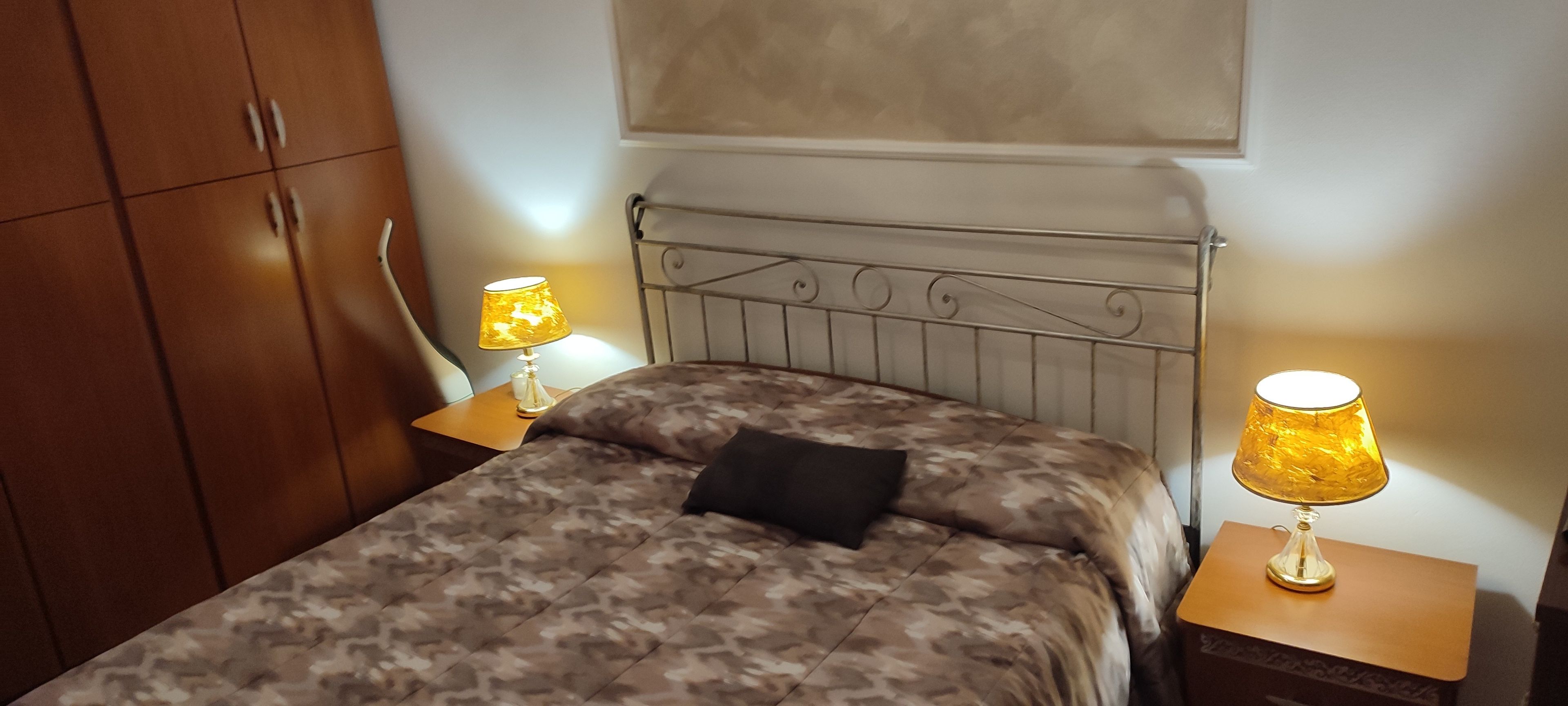 Ein Schlafzimmer mit einem Bett, zwei Nachttischlampen, einem Holzschrank und einem Wandregal.