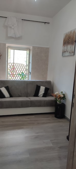 A living room with a grey sofa, a window with a view of greenery, and a wall-mounted artwork.