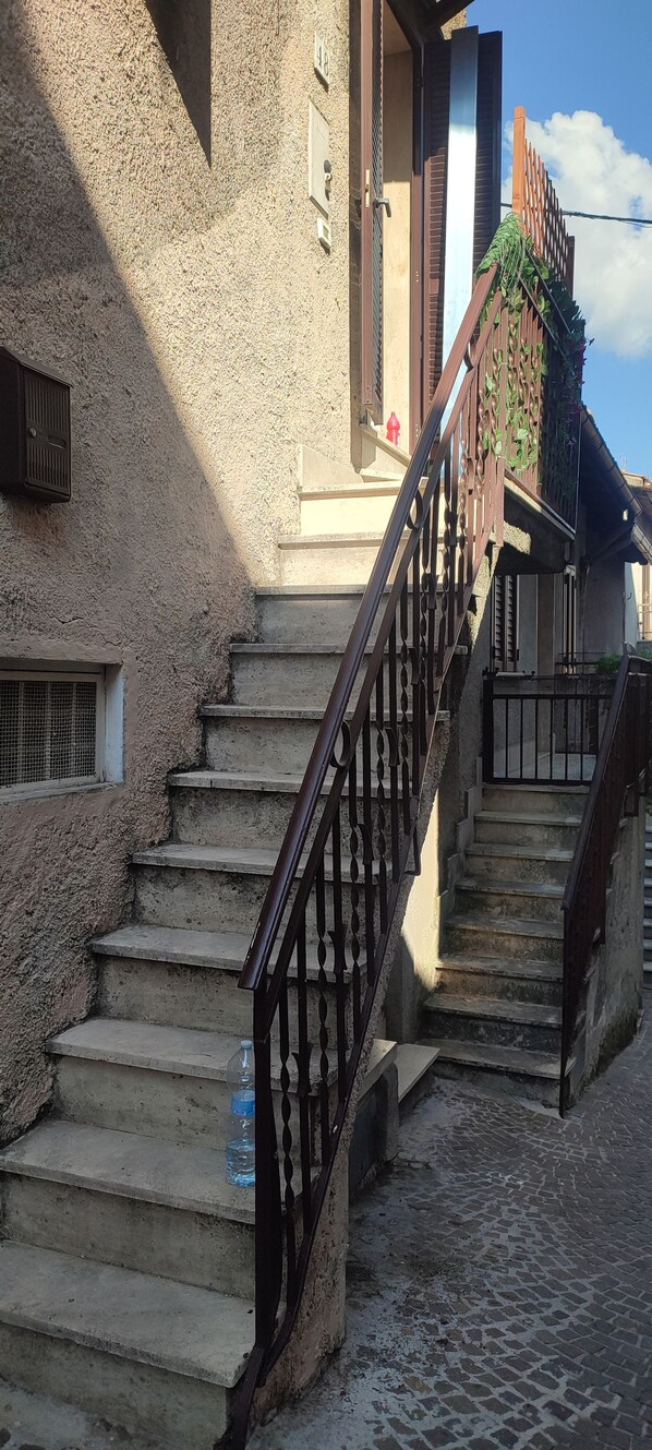 Una scala in pietra con ringhiere in metallo conduce a un edificio con una porta in legno e una finestra con inferriata.