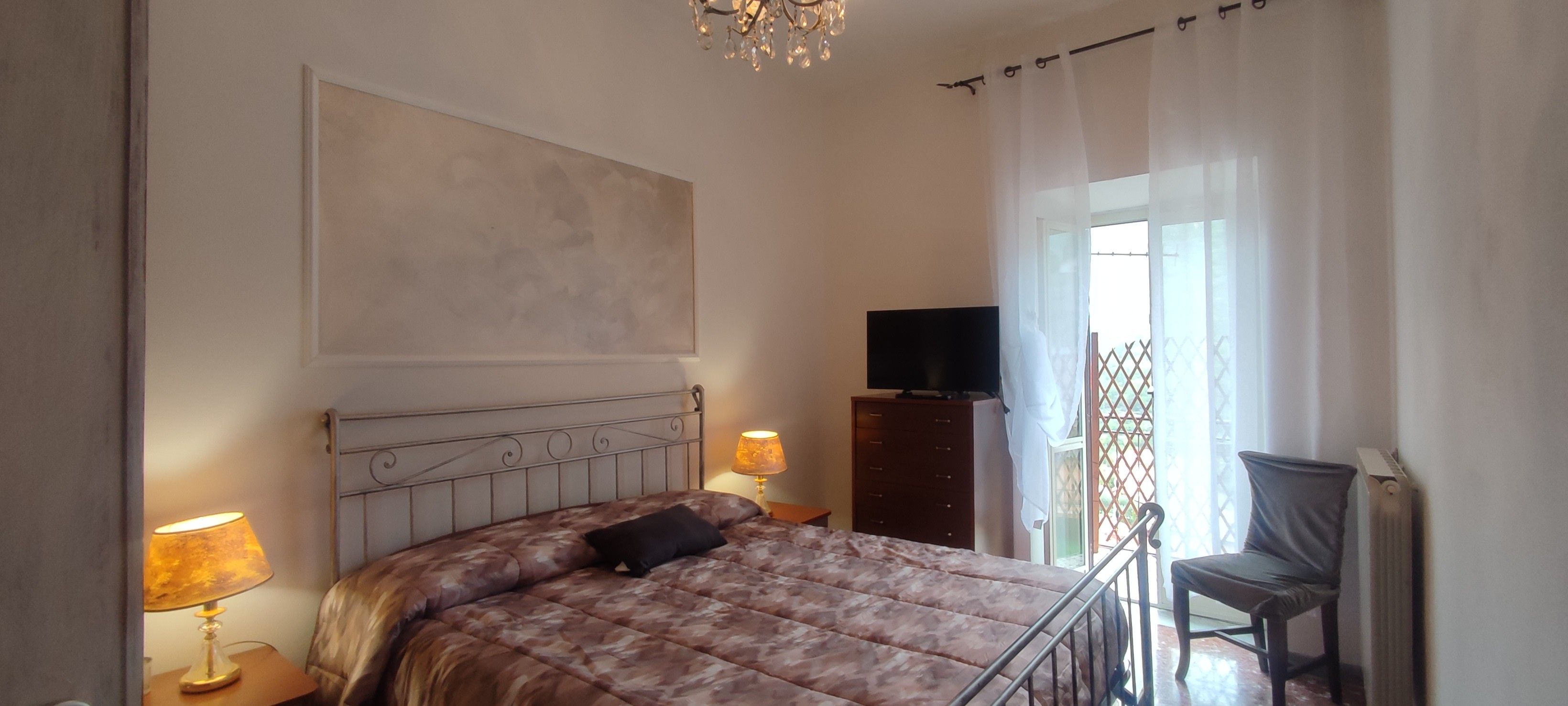 A bedroom with a bed, bedside lamps, a television on a stand, and a chair.
