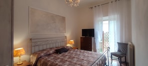 A bedroom with a bed, bedside lamps, a television on a stand, and a chair.
