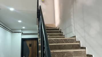 Una escalera con escalones de mármol y barandilla negra, que lleva a una puerta con panel de madera.